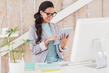 Businesswoman smiling while working on tablet in front of a computer